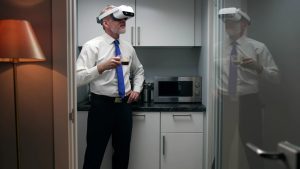 Muž má na sebe okuliare na virtuálnu realitu a pritom pije kávu v kuchyni