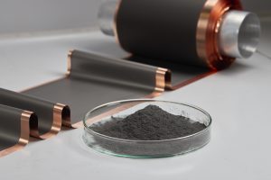 Čierny prášok v miske na bielom stole, v pozadí vrstvy batérie