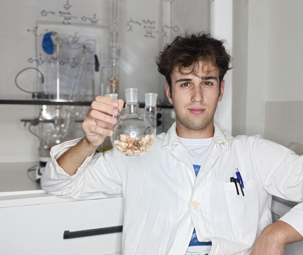 Mladý výskumník v bielom plášti pózuje s laboratórnou pomôckou