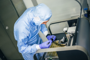 Výskumník v modrom ochrannom obleku a rukaviciach pri práci v laboratóriu