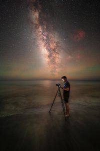 Fotograf s fotoaparátom na statíve fotografuje Mliečnu cestu