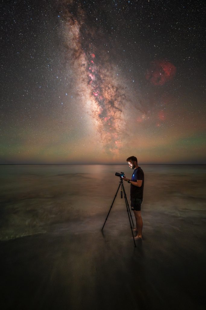 Fotograf s fotoaparátom na statíve fotografuje Mliečnu cestu