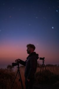 Muž s fotoaparátmi sa díva do diaľky počas súmraku