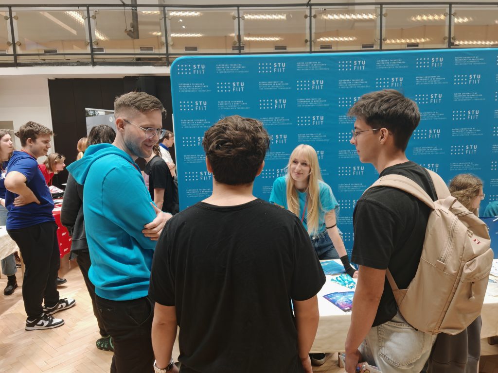 Skupina mladých ľudí sa rozpráva pri prezentačnom stánku FIIT STU.