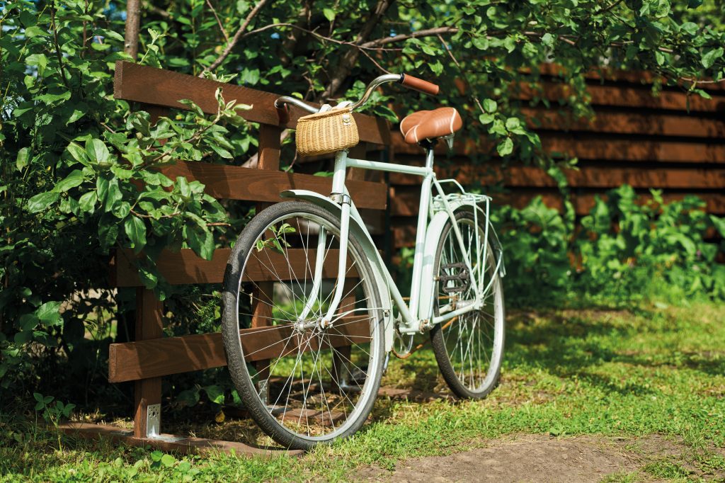 Biely bicykel s prúteným košíkom opretý o drevenú ohradu